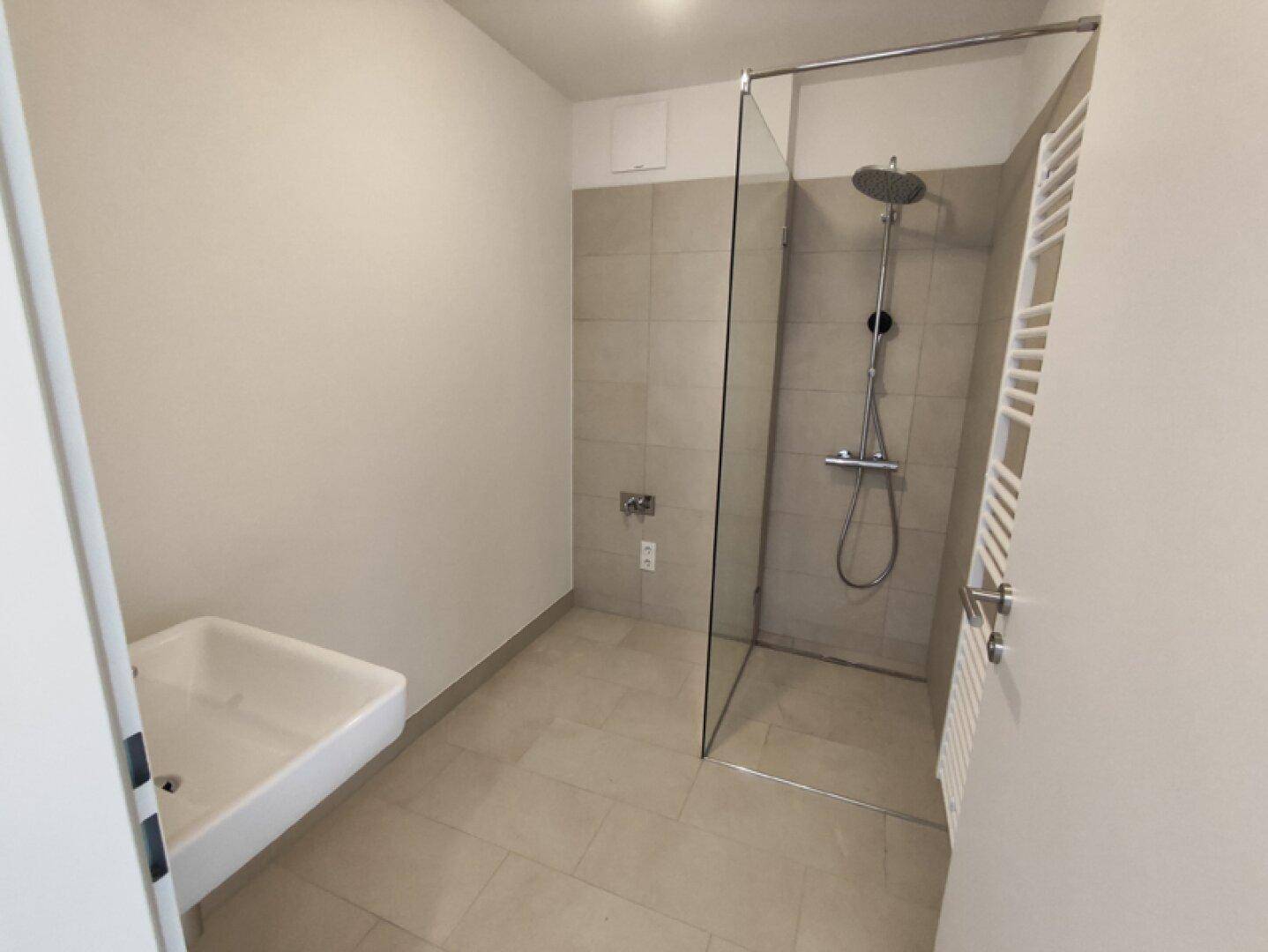 Modernes Badezimmer mit ebenerdiger Dusche, Einzelwaschbecken und beheiztem Handtuchhalter.