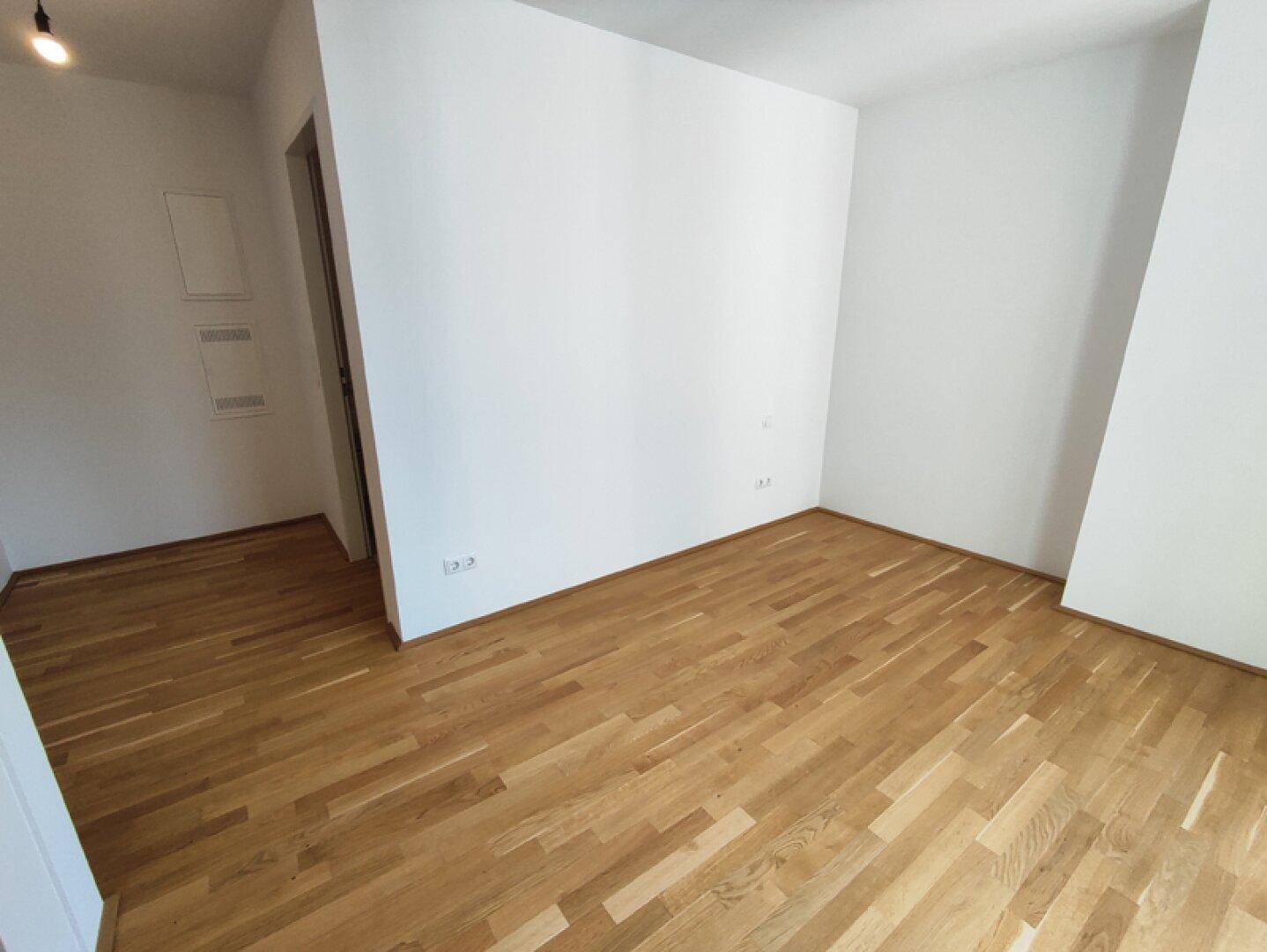 Leerer Raum mit hellem Parkettboden und weißen Wänden, bereit für die individuelle Gestaltung.