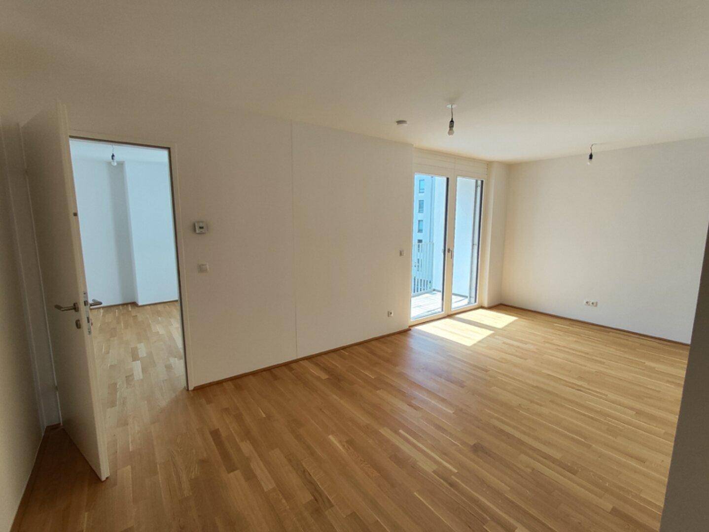 Heller, leerer Wohnraum mit Parkettboden und Zugang zu einem Balkon, bereit zur Einrichtung.
