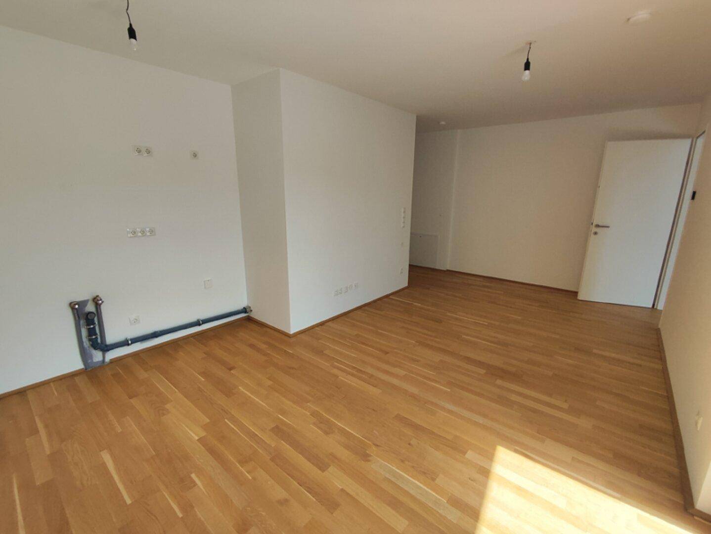 Heller Raum mit Parkettboden und weißen Wänden, vorbereitet für Kücheninstallationen.