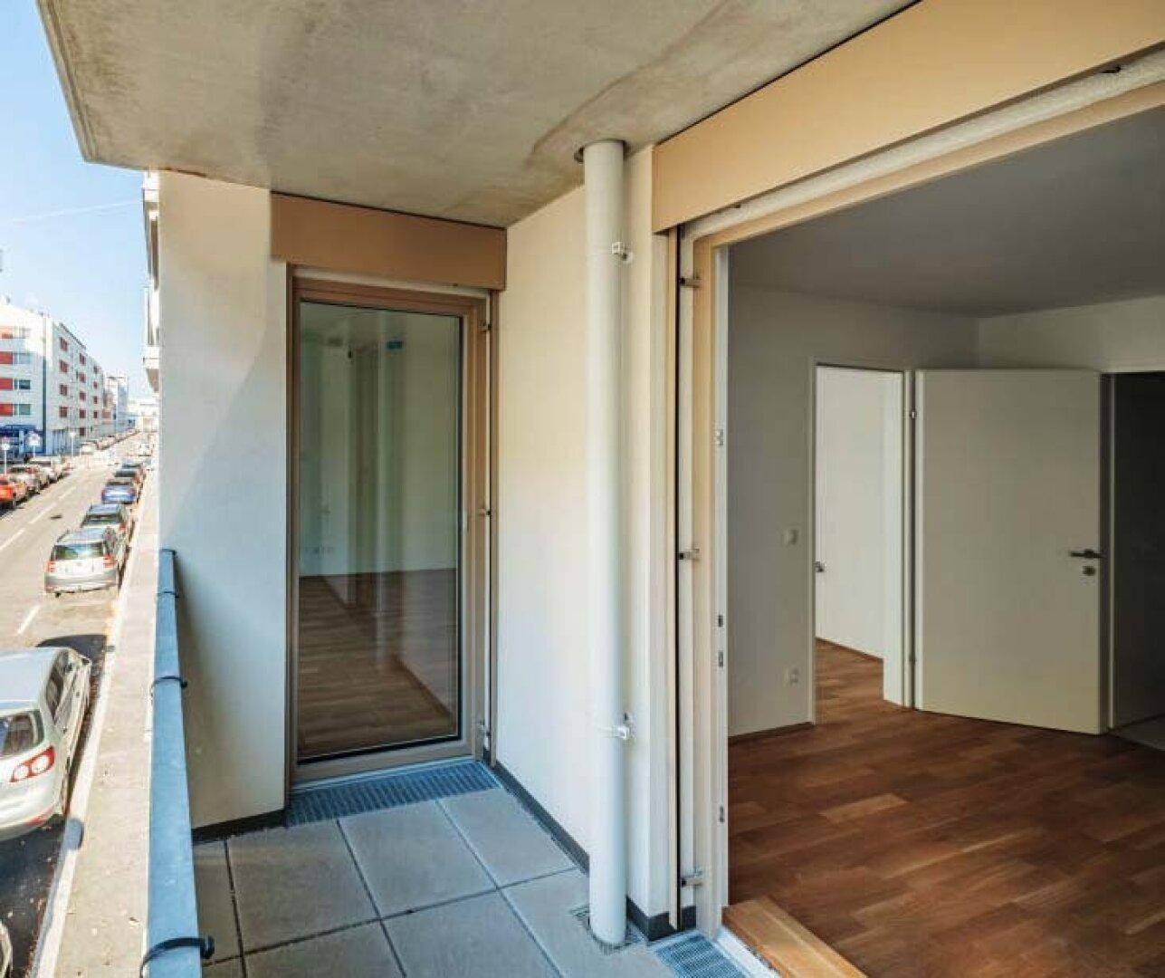Balkon mit Fliesenboden und Blick auf die Straße und umliegende Gebäude.