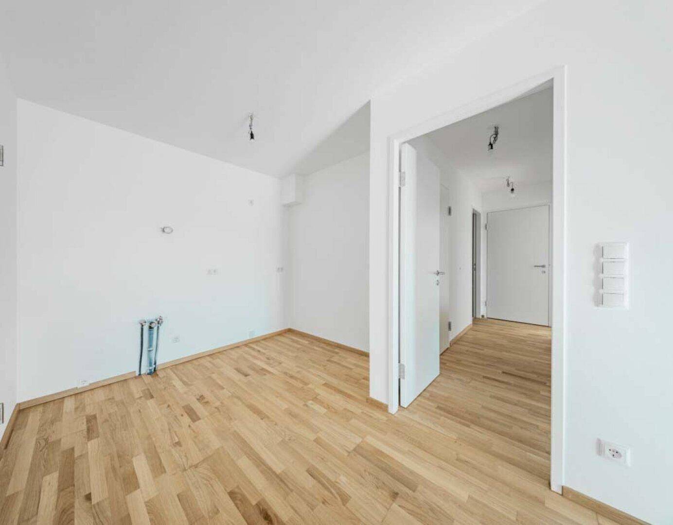 Leerer Raum mit Anschlüssen für eine Küche und Holzboden, bereit für die Installation.