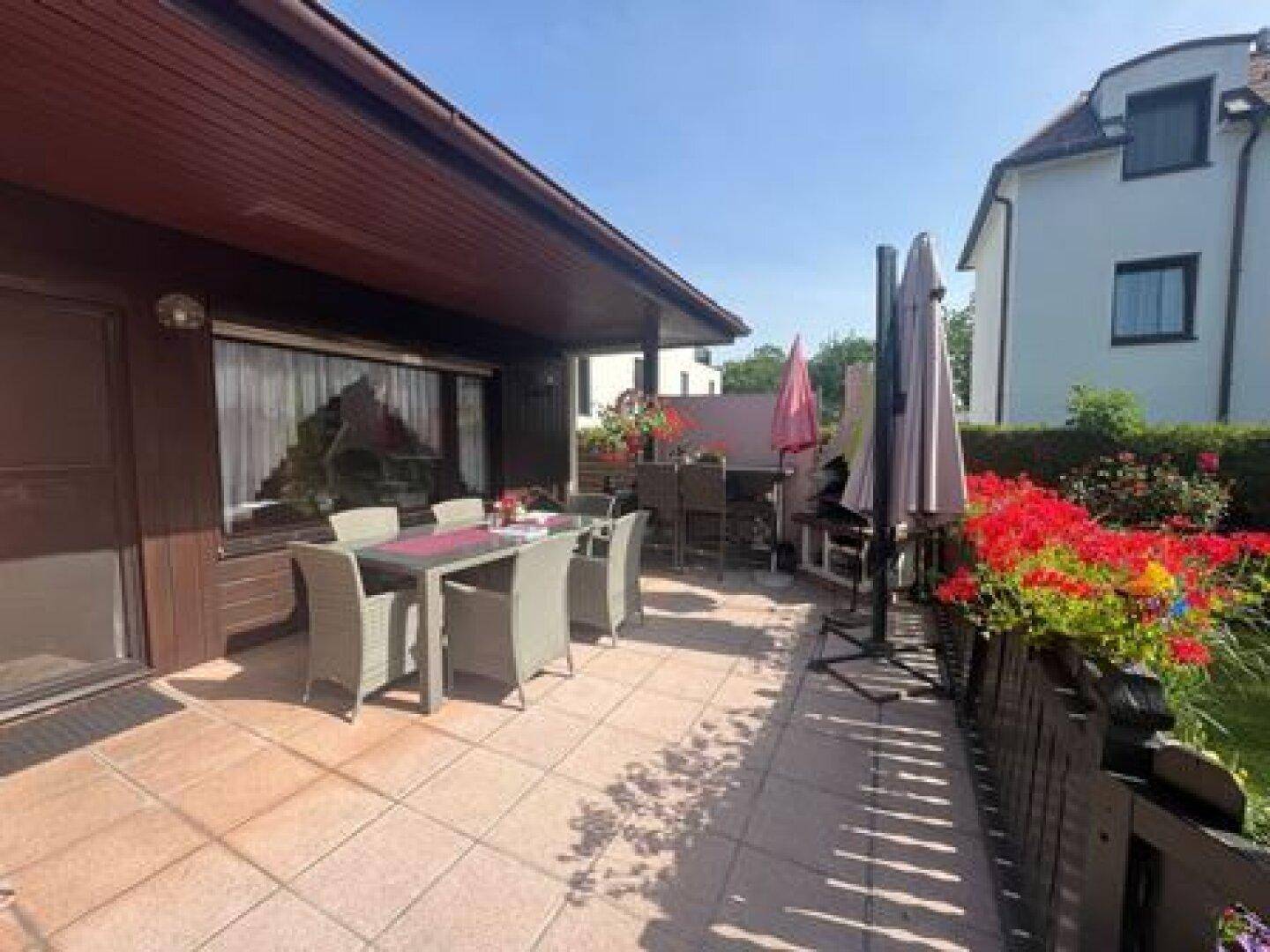 Geräumige, geflieste Terrasse mit Gartenmöbeln und Blick auf den gepflegten Gartenbereich.