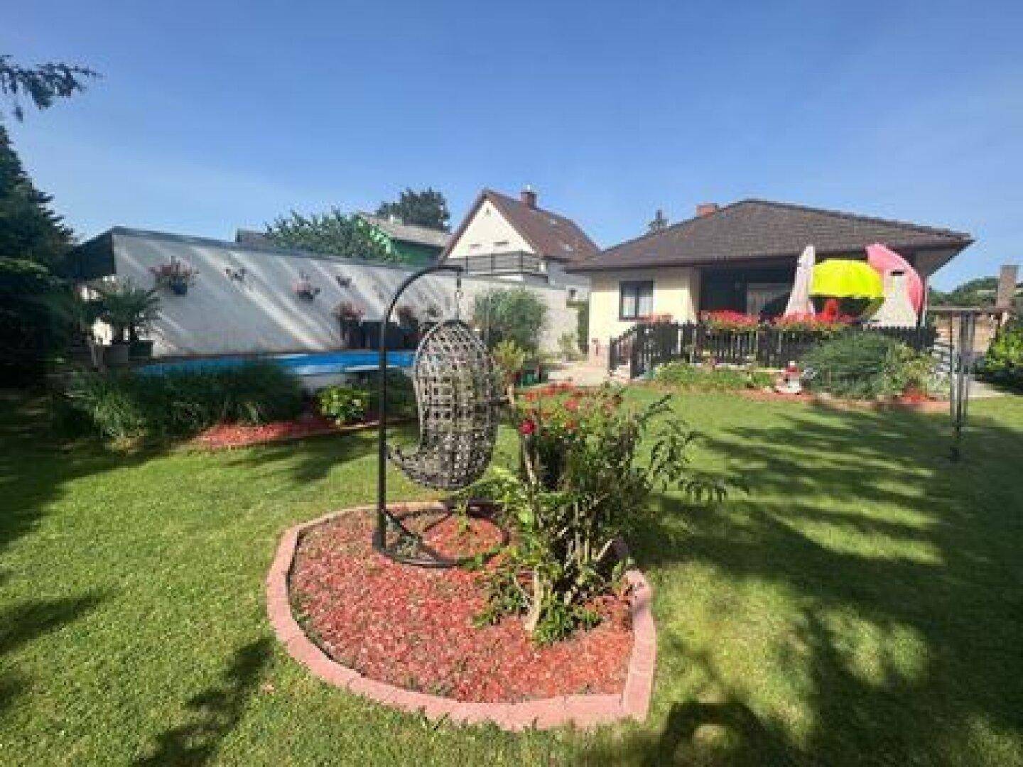 Großer Garten mit Rasenfläche, Hängesessel und einem sichtbaren Pool im Hintergrund.