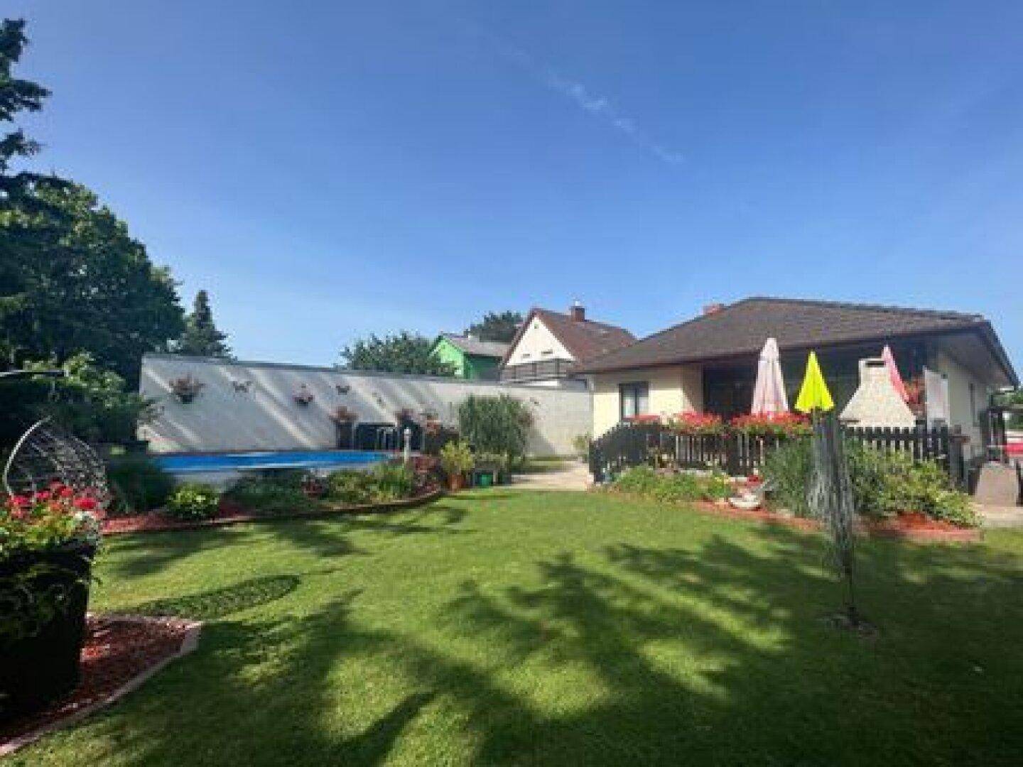 Panoramablick auf den weitläufigen Garten mit Pool, Terrasse und dem Haus im Hintergrund.