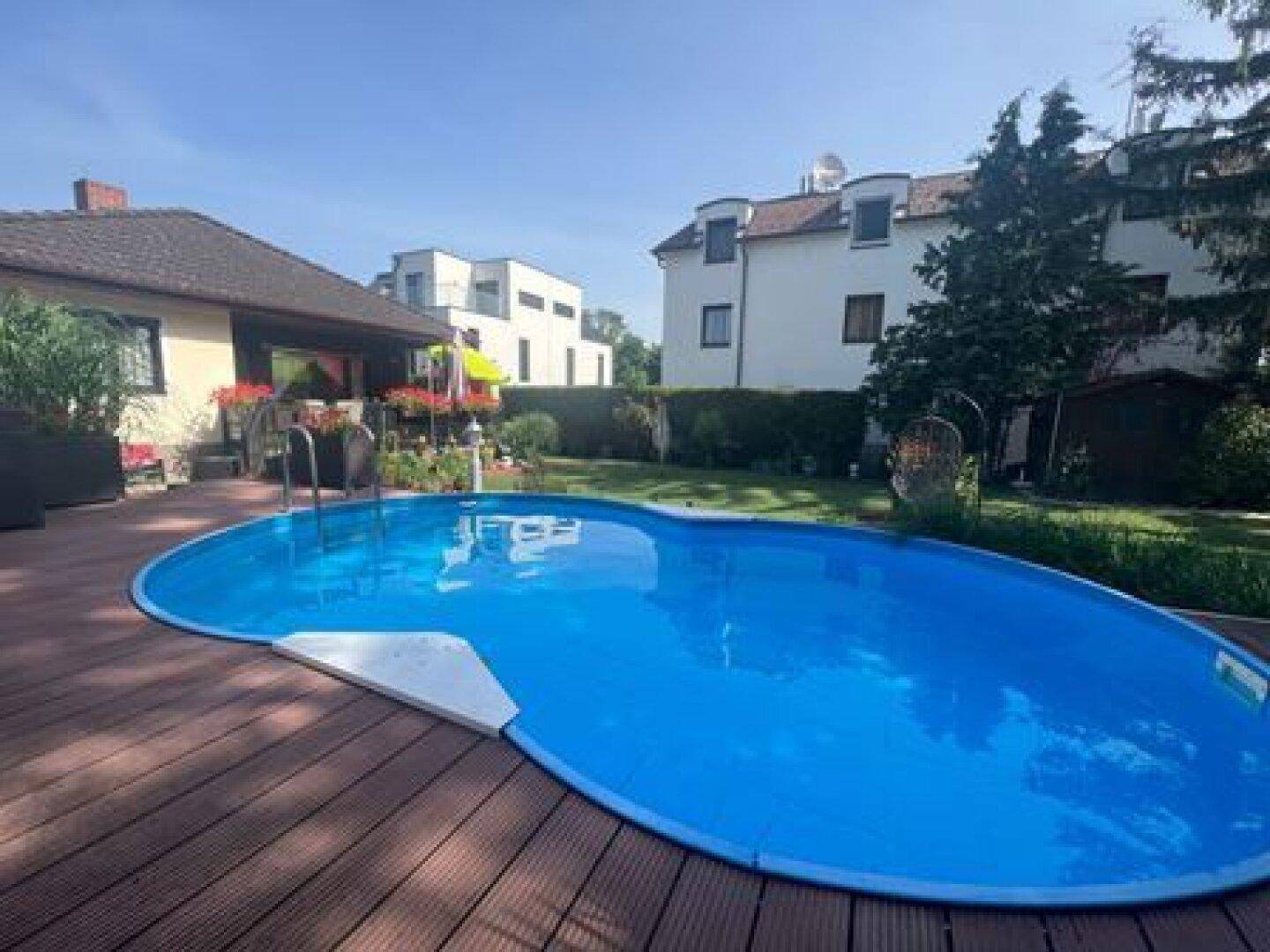 Weitläufiger Garten mit großem Pool und Holzdeck, umgeben von Nachbarhäusern und Bäumen.