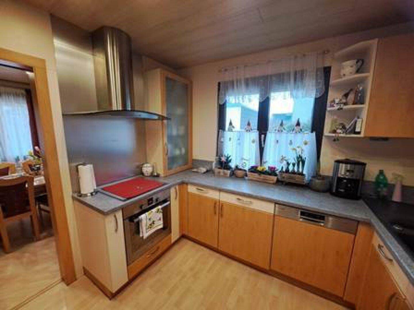 Funktionale Küche mit Holzfronten, Dunstabzugshaube, Backofen und Fenster mit Vorhängen.