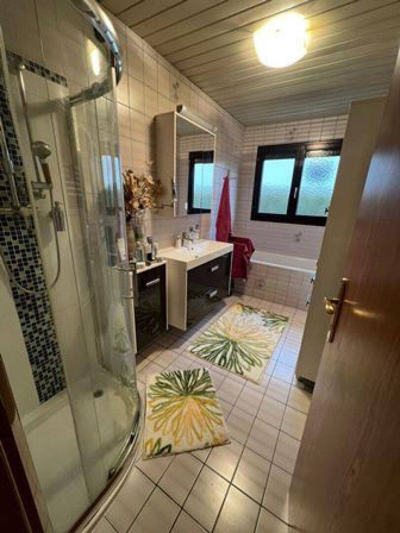 Badezimmer mit Duschkabine, Badewanne, Waschbecken und hellen Fliesen an den Wänden.