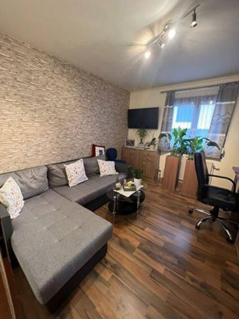 Gemütliches Wohnzimmer mit Ecksofa, strukturierten Wänden und dunklem Holzboden.