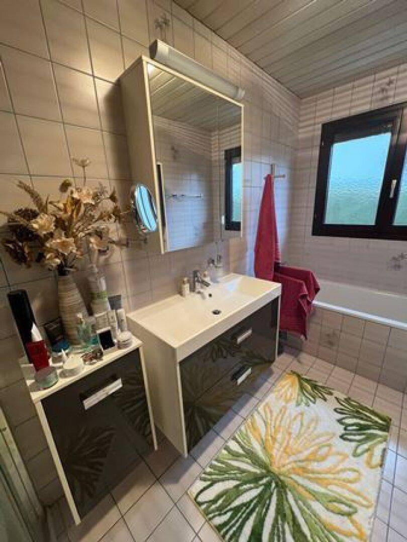 Modernes Badezimmer mit Waschbeckenunterschrank, Spiegel und Badewanne im Hintergrund.