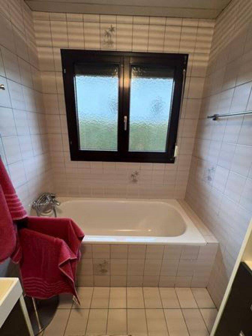 Helles Badezimmer mit Badewanne, Fliesenboden und einem Fenster für Tageslicht.