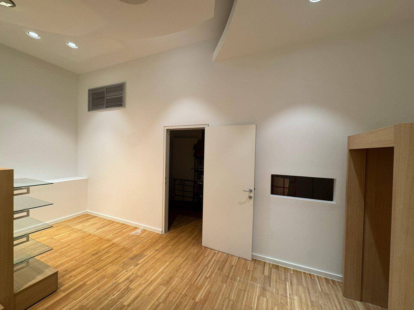 Detailansicht eines Ladenlokals mit einer Tür, Lüftungsgitter und einem eingebauten Regal an der Wand.