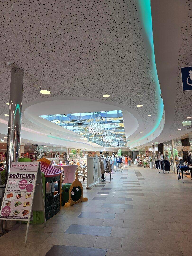 Weitläufige Einkaufspassage mit hellem Tageslicht durch ein großes Oberlicht und vielfältigen Geschäften.