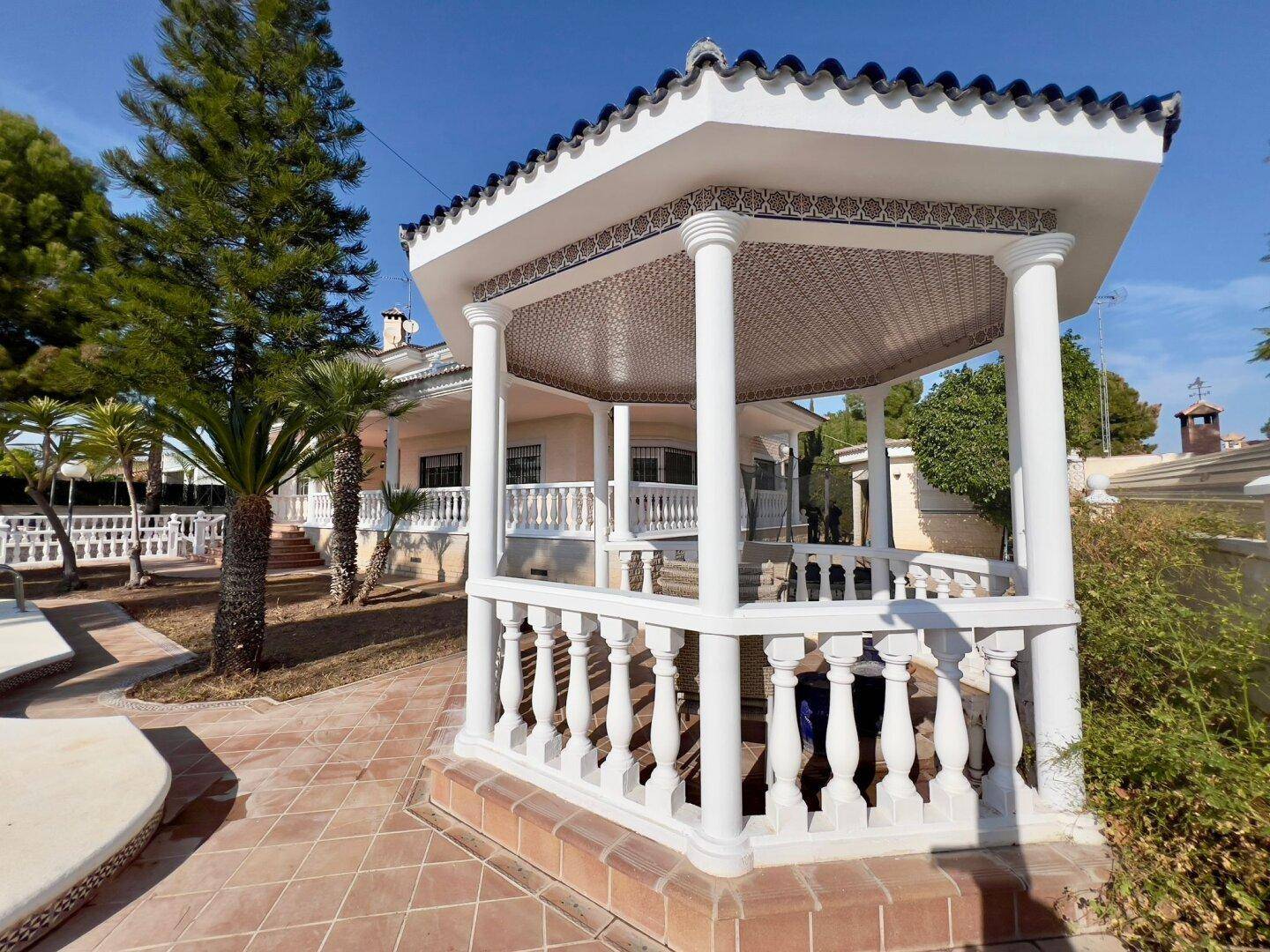 Ein charmanter Pavillon mit Säulen und gefliestem Dach, umgeben von einem gefliesten Bereich im Garten.