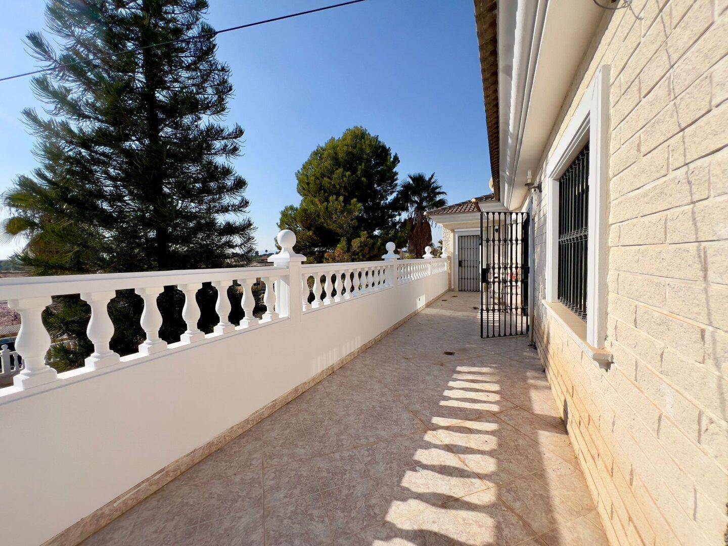 Langer Balkon mit Fliesenboden und weißer Balustrade, der sich entlang der Hausfassade erstreckt.