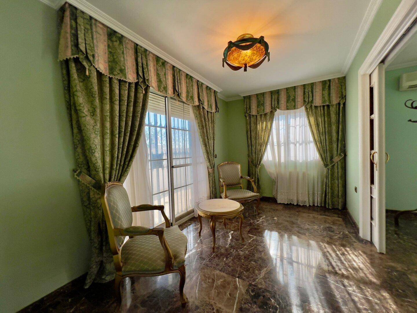 Gemütliche Sitzecke mit eleganten Sesseln, grünen Vorhängen und glänzendem Marmorboden.