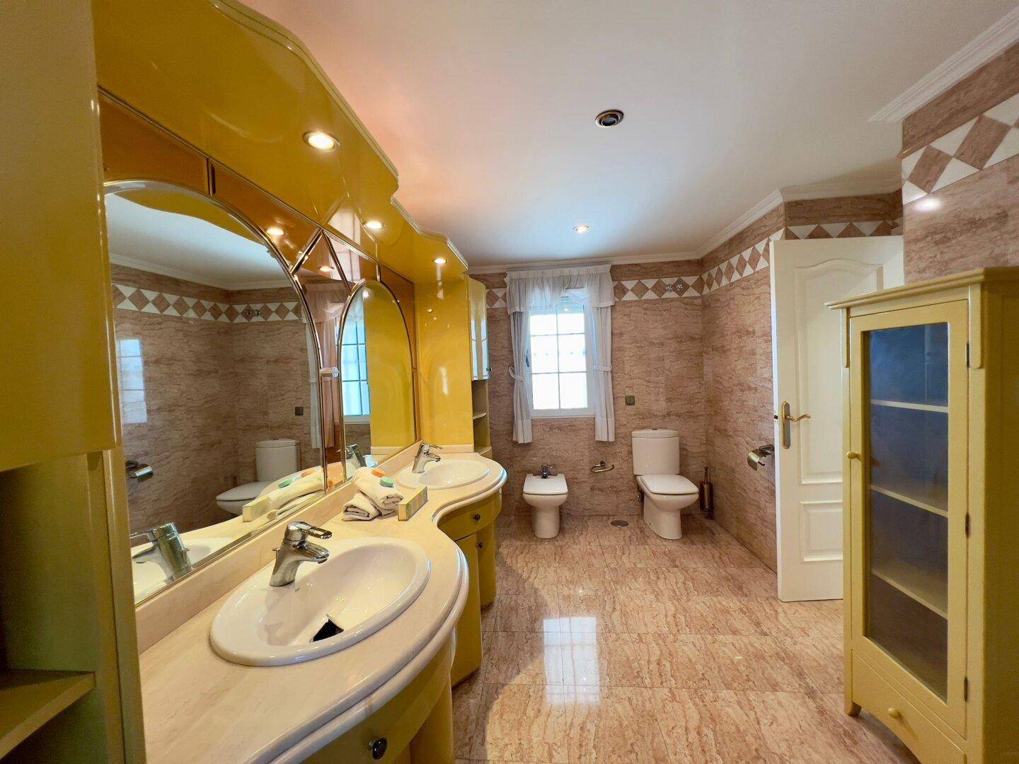 Geräumiges Badezimmer mit gelben Waschtischen, großer Badewanne, Bidet und WC.