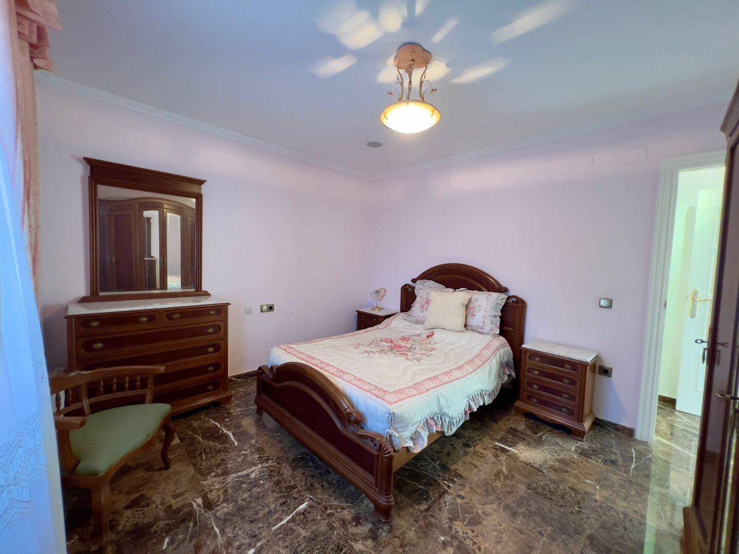 Helles Schlafzimmer mit traditionellem Bett, passender Kommode und rosa Wänden.