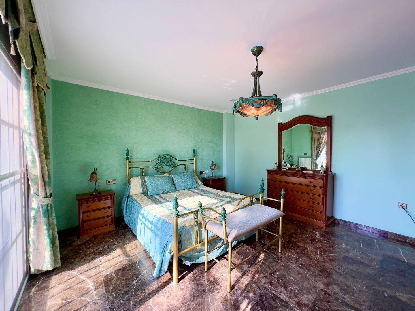 Helles Schlafzimmer mit klassischem Bettgestell, grünen Wänden und direktem Zugang zum Außenbereich.