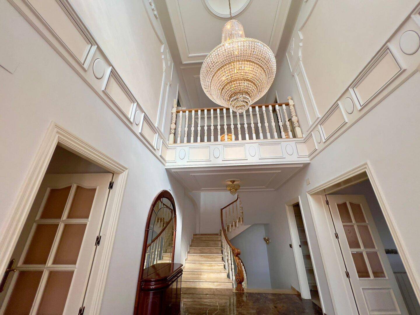 Beeindruckende Eingangshalle mit hoher Decke, großem Kronleuchter und geschwungener Treppe.