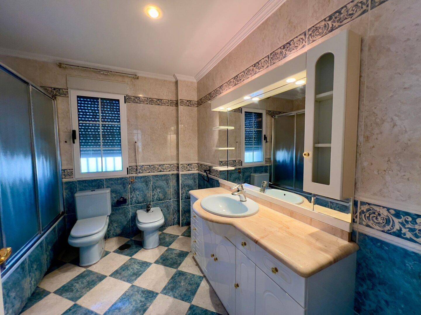 Badezimmer mit blauen und beigen Fliesen, Waschtisch mit Spiegelschrank und Duschkabine.