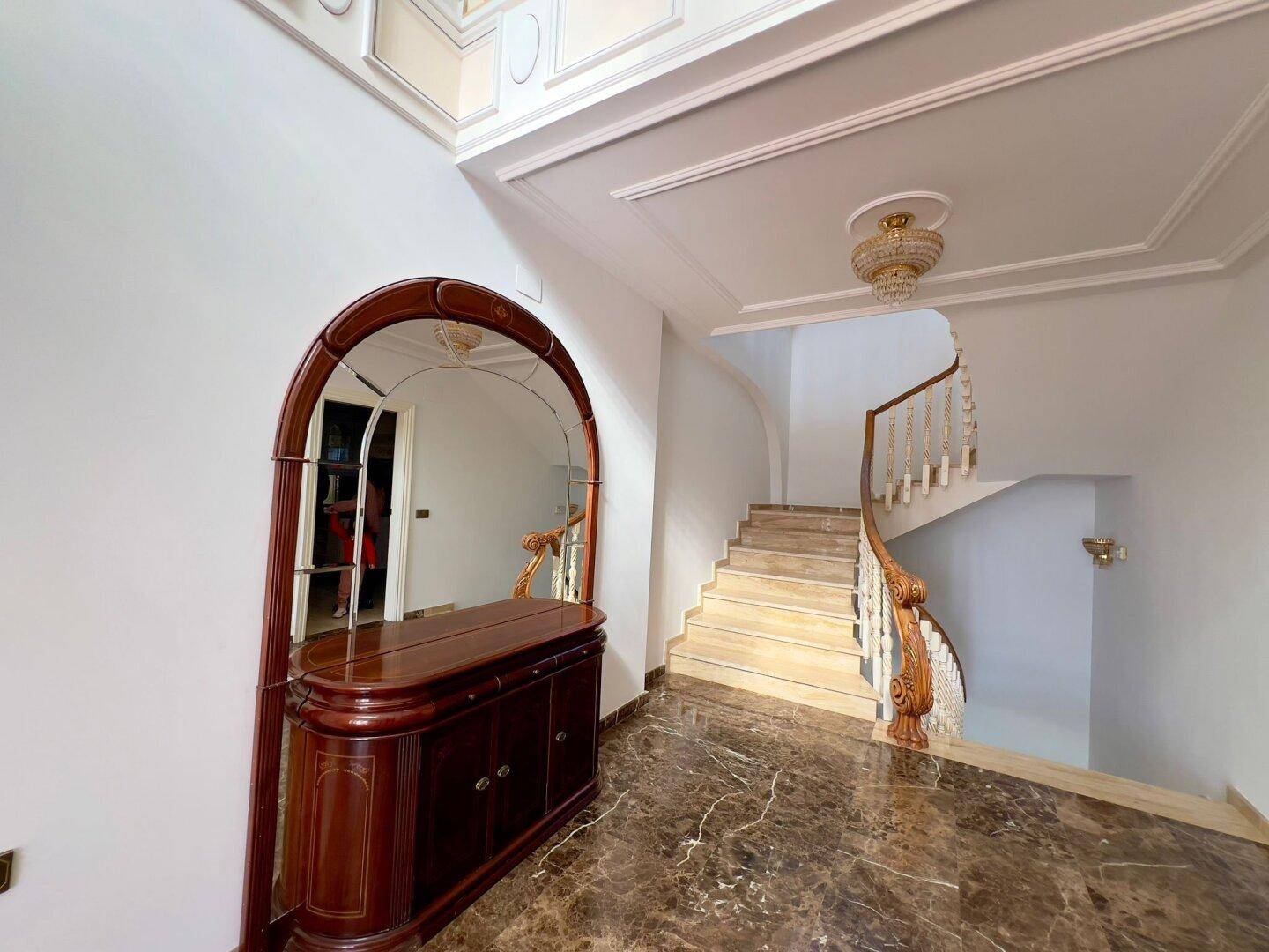 Elegante Eingangshalle mit großem Spiegel, Marmorboden und geschwungener Treppe.