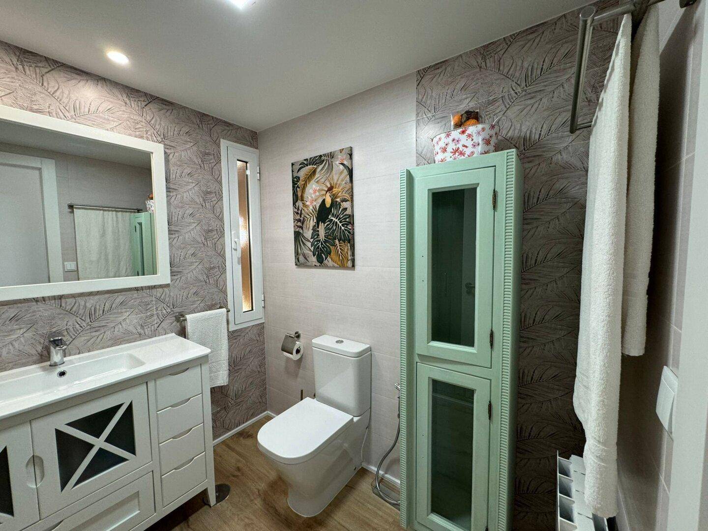 Badezimmer mit Waschtisch, Toilette und auffälligen Wandfliesen mit Pflanzenmuster.