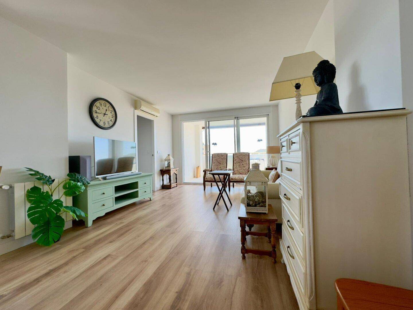 Lichtdurchfluteter Wohnbereich mit Holzboden, TV und großem Fenster mit Zugang zum Balkon.