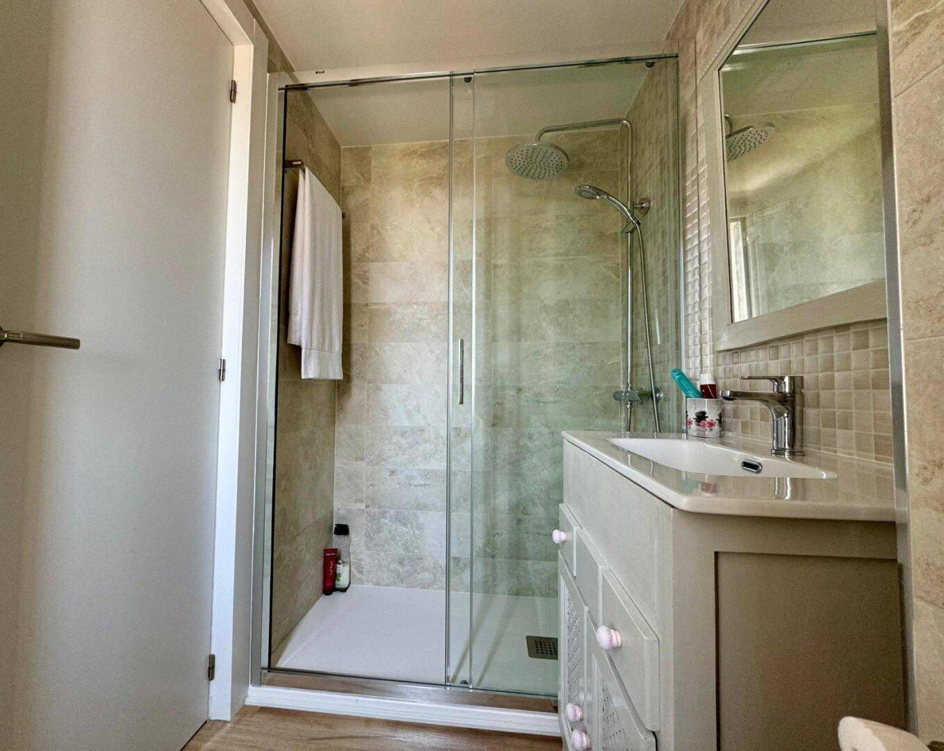 Modernes Badezimmer mit Duschkabine, Regendusche, Waschtisch und beigen Wandfliesen.