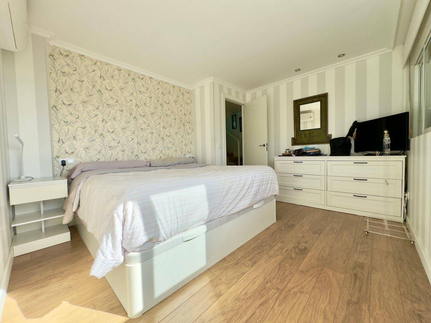 Helles Schlafzimmer mit Holzboden, gestreiften Wänden und einem großen Bett.