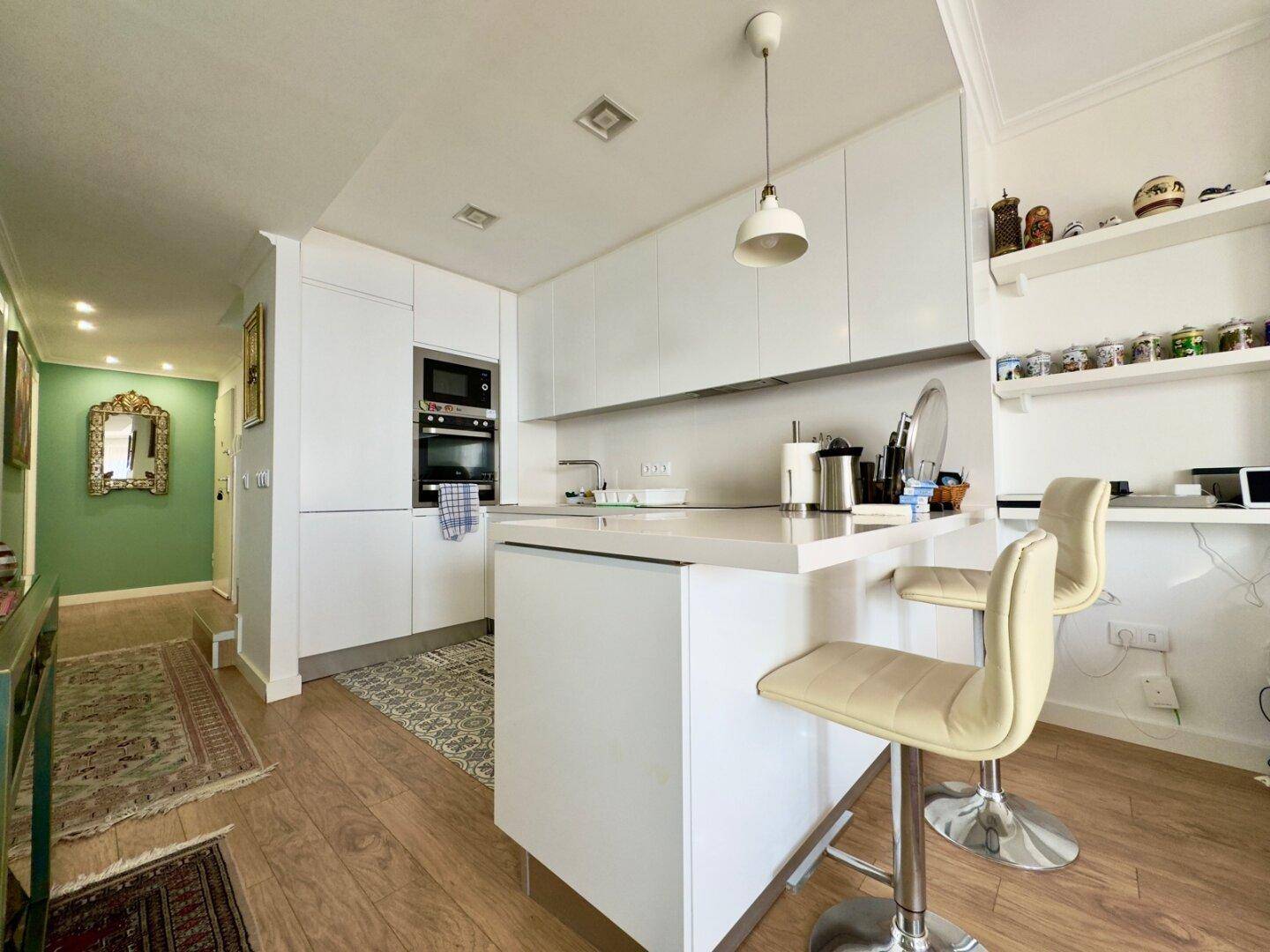 Moderne weiße Küche mit Kücheninsel, Barhockern und Holzboden.
