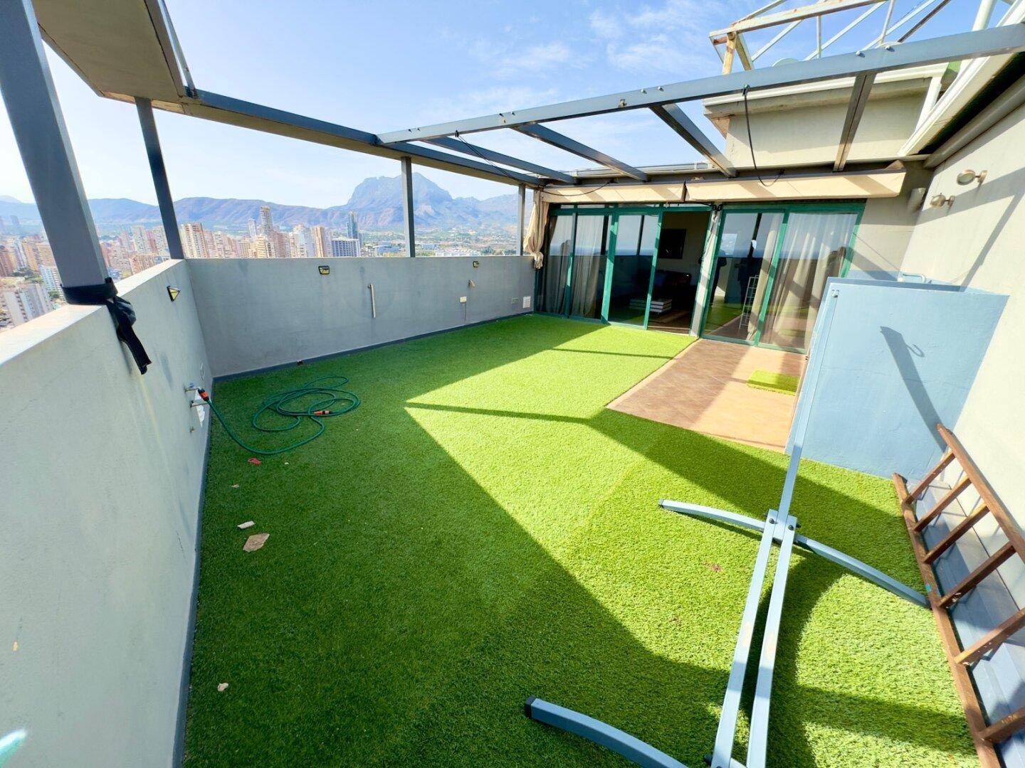 Weitläufige Dachterrasse mit Kunstrasen, Pergola und Panoramablick auf die Stadt und das Meer.