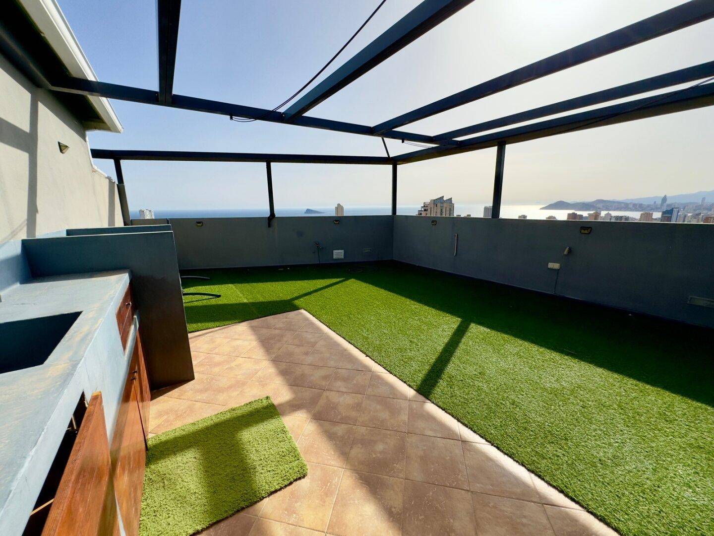 Sonniger Dachterrassenbereich mit Kunstrasen, Außenküche und weitem Meerblick.