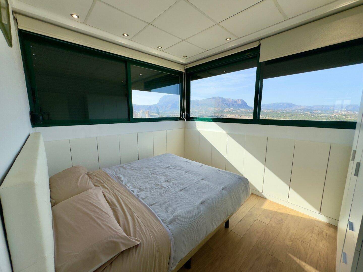 Schlafzimmer mit Bergblick, Holzboden und Einbauschränken unter den Fenstern.