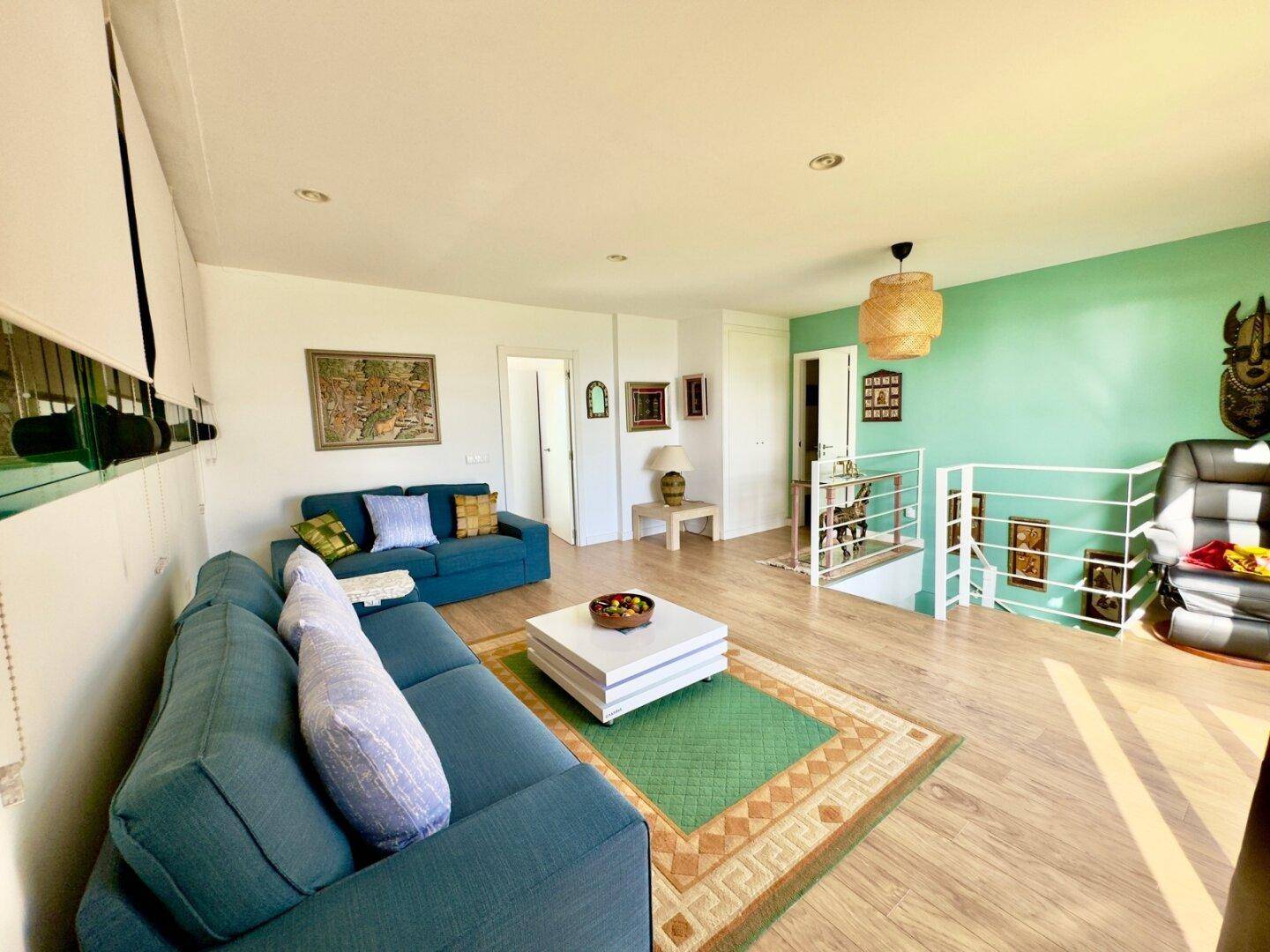Geräumiges Wohnzimmer mit blauen Sofas, Holzboden und farbenfroher Dekoration.