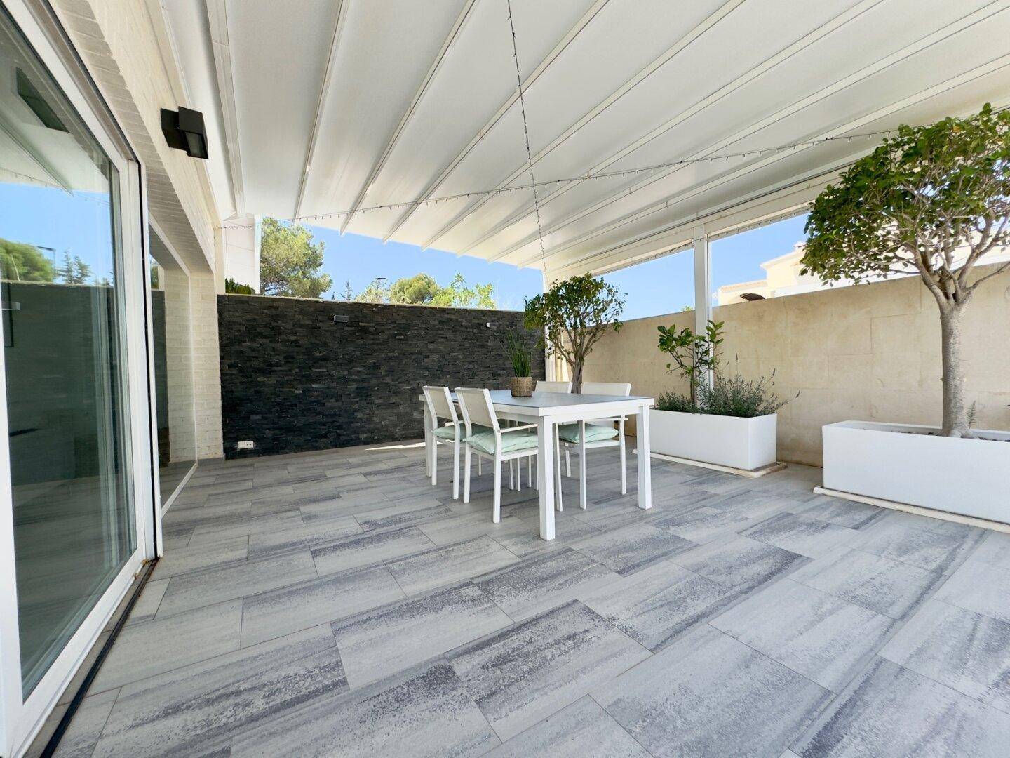 Große überdachte Terrasse mit Essbereich und modernen Fliesen, ideal für Mahlzeiten im Freien.