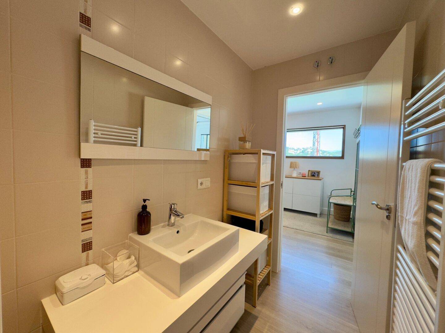 Modernes Badezimmer mit Waschtisch, Spiegel und beheiztem Handtuchhalter an der Wand.