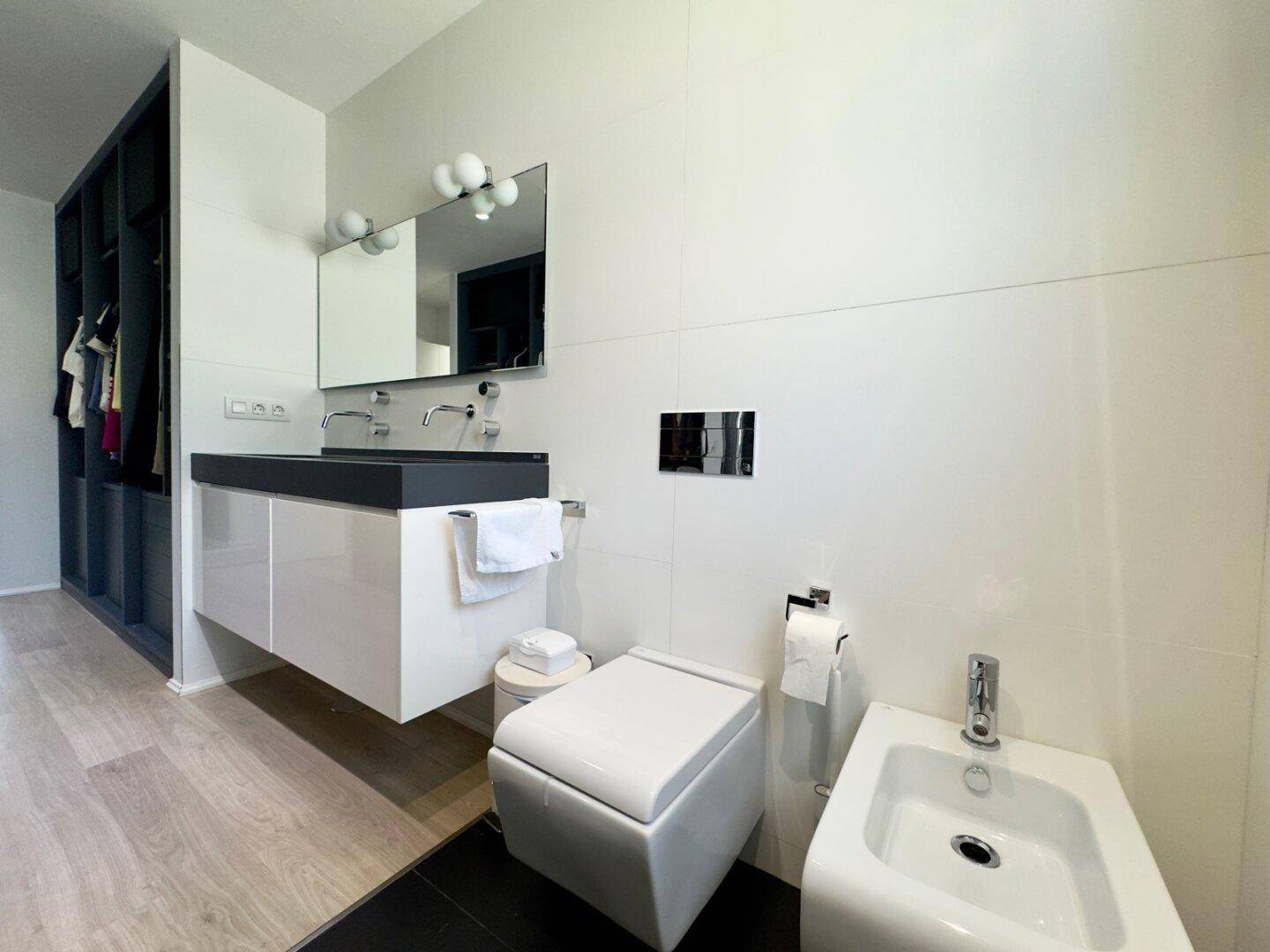 Helles Badezimmer mit Bidet, Wand-WC und Doppelwaschbecken in modernem Design.