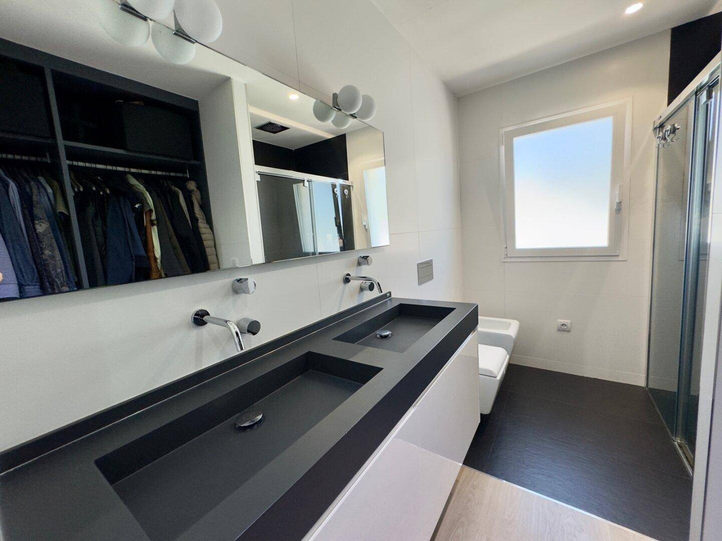 Modernes Badezimmer mit Doppelwaschbecken, großer Dusche und Fenster für Tageslicht.