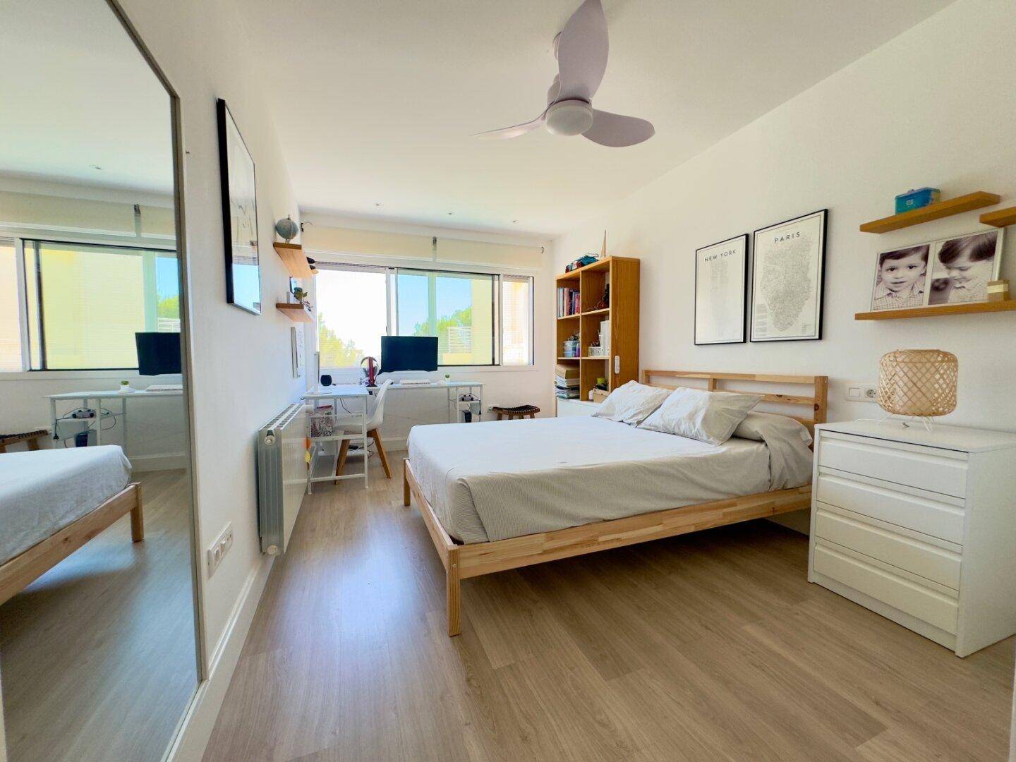 Helles Schlafzimmer mit Arbeitsbereich, großem Fenster und Deckenventilator für angenehmes Klima.