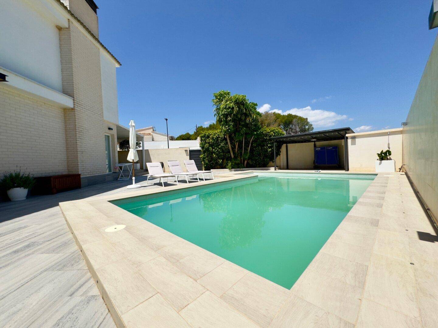 Großer Swimmingpool mit Liegebereich unter strahlend blauem Himmel.