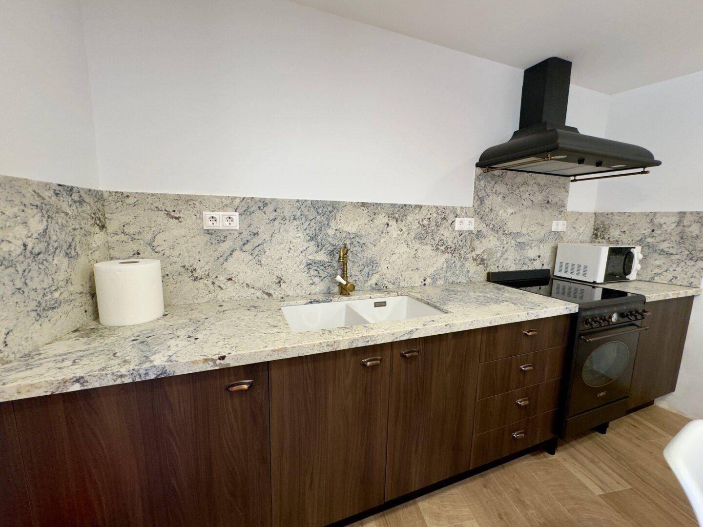 Funktionale Küche mit Granitarbeitsplatte, Holzschränken und Dunstabzugshaube.