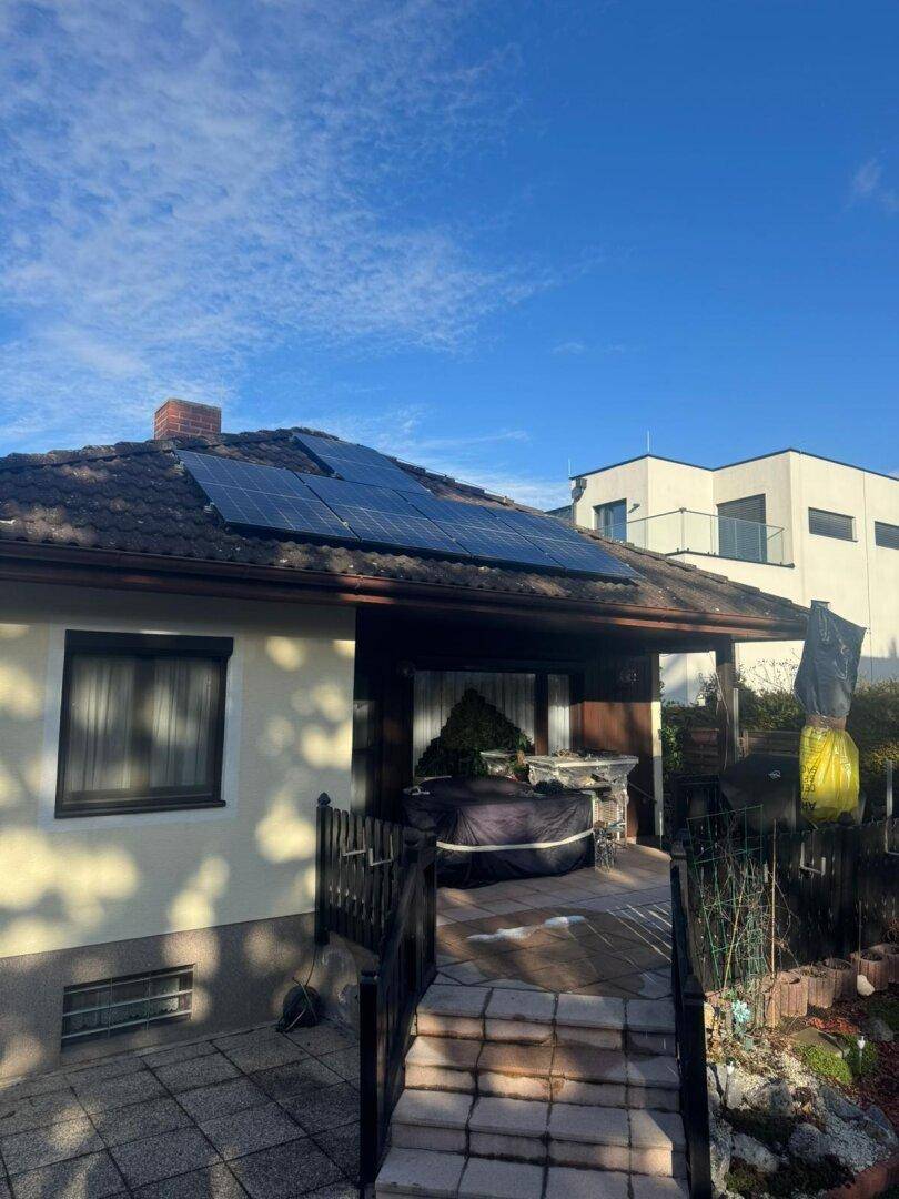 Außenansicht des Hauses mit Solarmodulen auf dem Dach und einem gepflasterten Terrassenzugang.