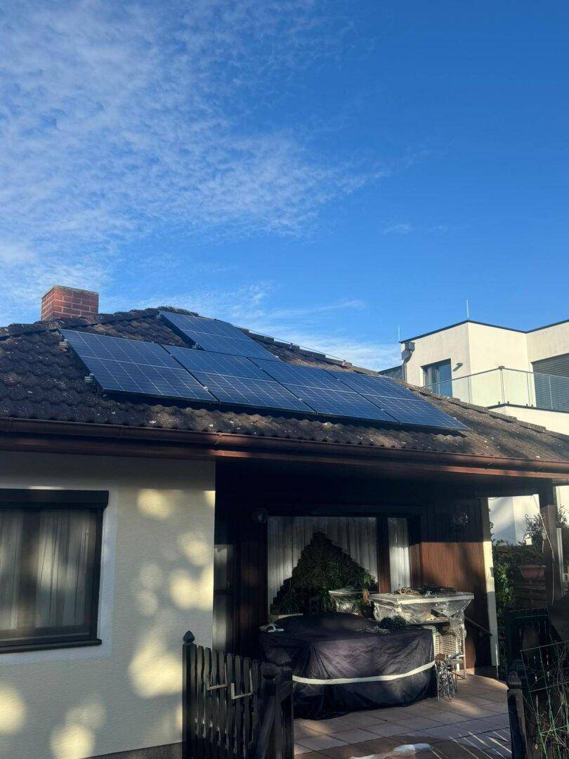 Hausfassade mit Photovoltaikanlage auf dem Dach und einem überdachten Terrassenbereich.