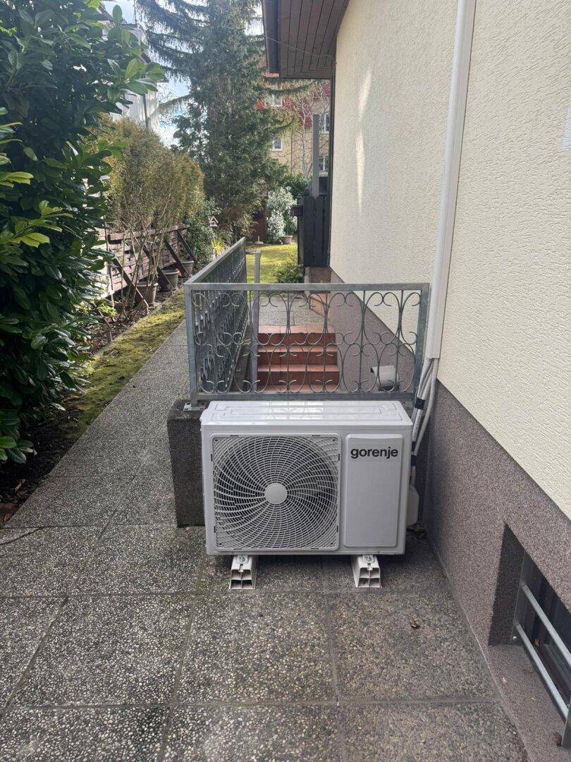 Außenansicht mit einer Gorenje Klimaanlage und einem gepflasterten Weg entlang des Hauses.