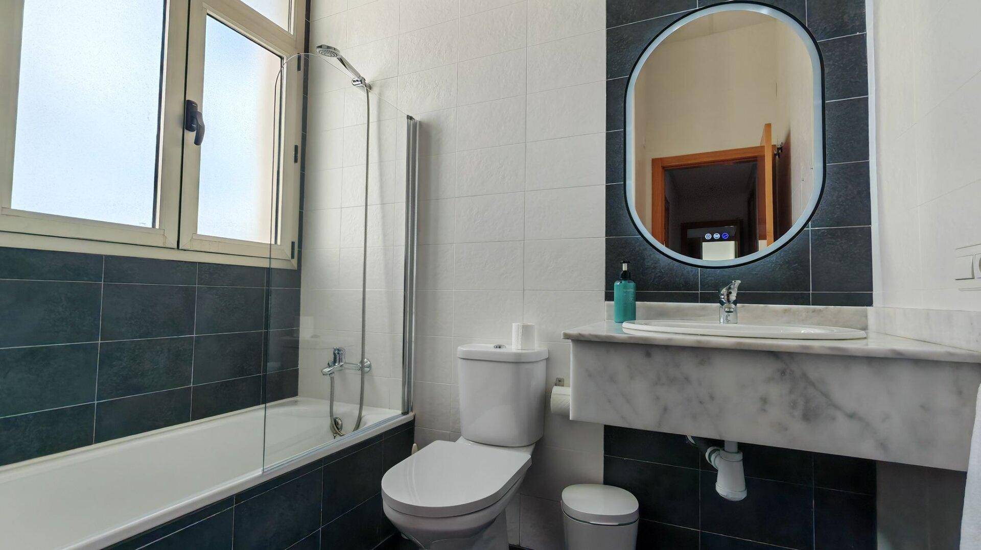 Modernes Badezimmer mit Badewanne, Duschabtrennung, Marmorwaschtisch und Fenster für Tageslicht.