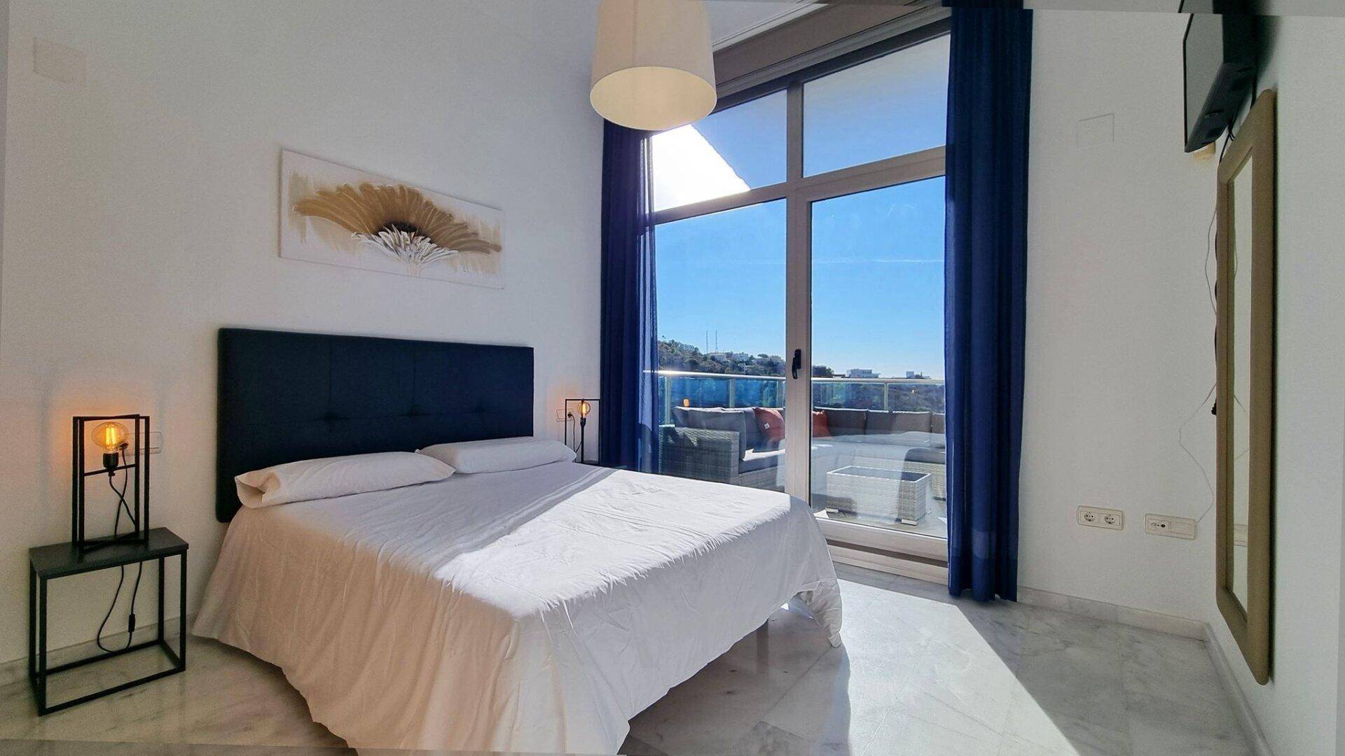 Helles Schlafzimmer mit Doppelbett, großen Fenstern und Zugang zu einem Außenbereich mit Meerblick.