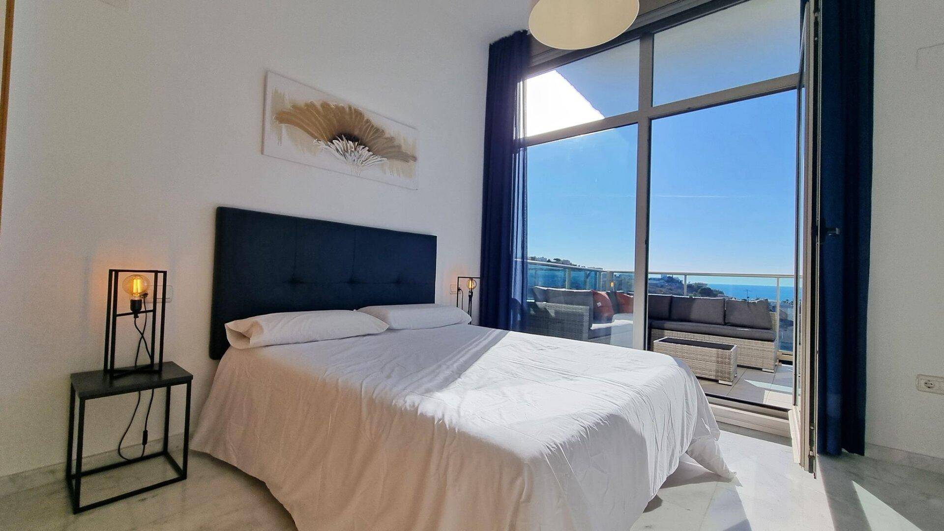 Geräumiges Schlafzimmer mit großem Bett, raumhohen Fenstern und direktem Zugang zum Balkon mit Meerblick.