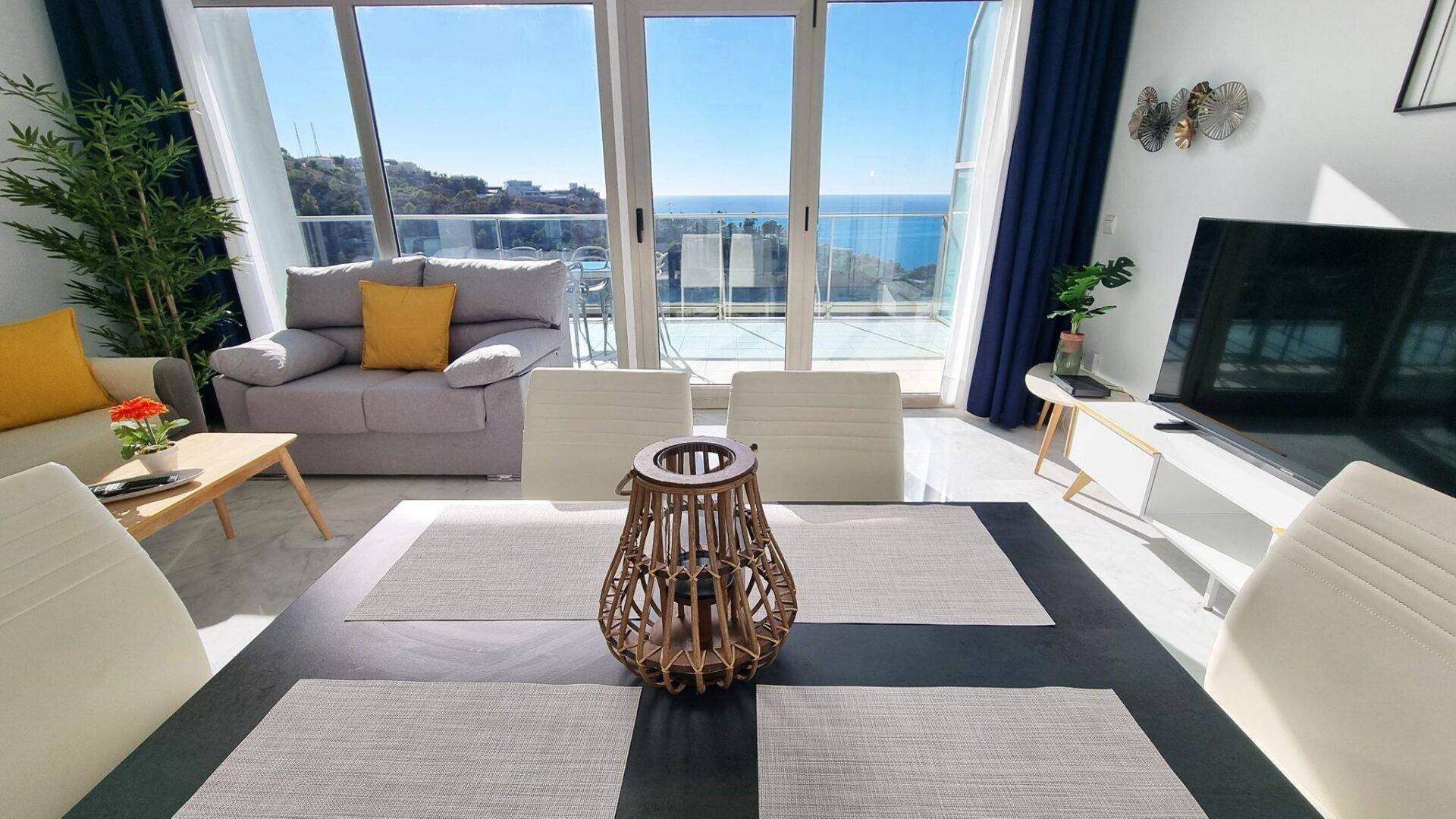 Moderner Essbereich im offenen Wohnraum mit Blick auf das Meer durch die großen Fenster.