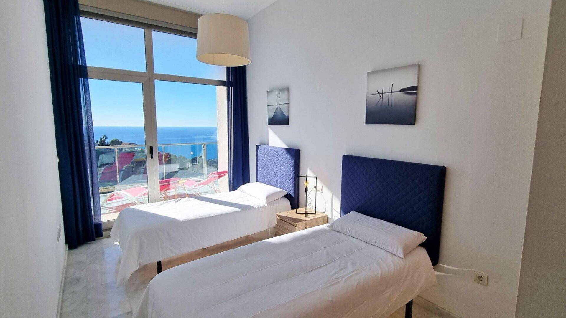 Schlafzimmer mit zwei Einzelbetten und großen Fenstern, die einen weiten Blick auf das Meer bieten.